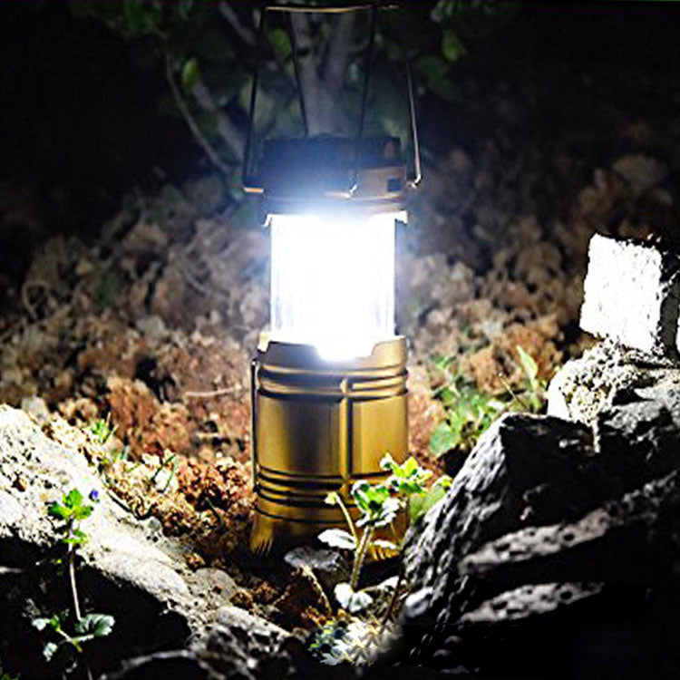 Camping lantern emitting light in a natural setting with rocks and plants.